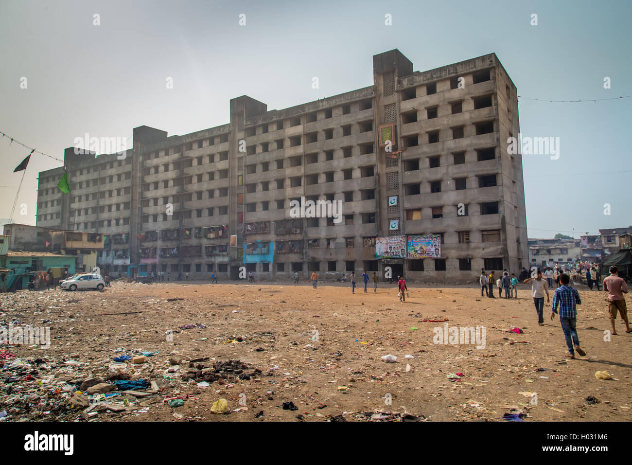 MUMBAI, INDIA - 12 JANUARY 2015: Unfinished empty apartment block and dirty field with people in Dharavi slum. Dharavi is one of Stock Photo