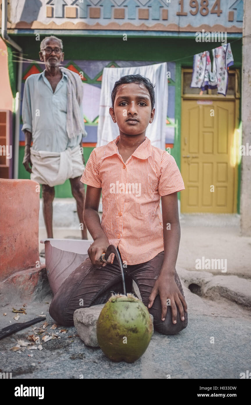 KAMALAPURAM, INDIA - 02 FABRUARY 2015: Indian boy opening a coconut in-front of house in a town close to Hampi. Post-processed w Stock Photo