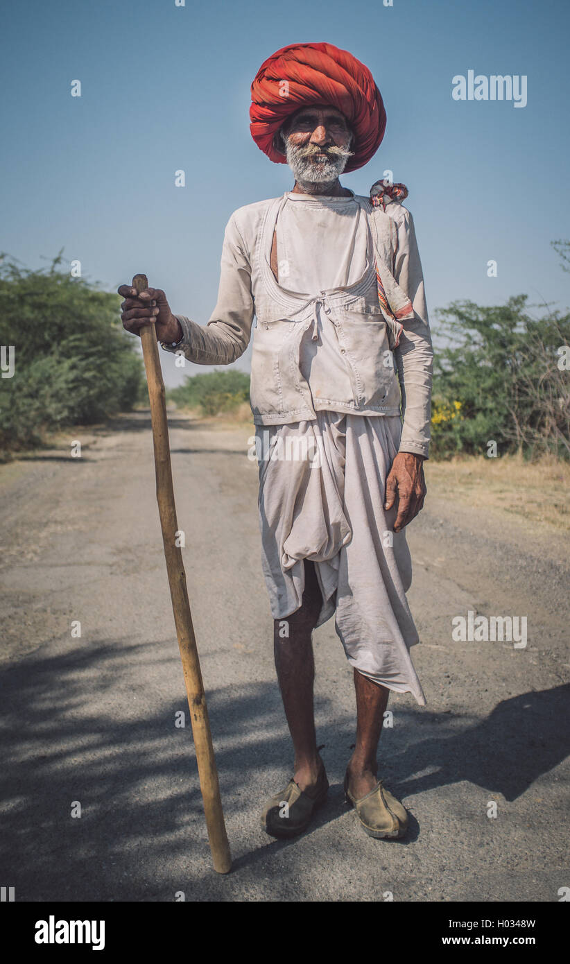 GODWAR REGION, INDIA - 14 FEBRUARY 2015: Elderly Rabari tribesman with big red turban and cane stands on road. Post-processed wi Stock Photo