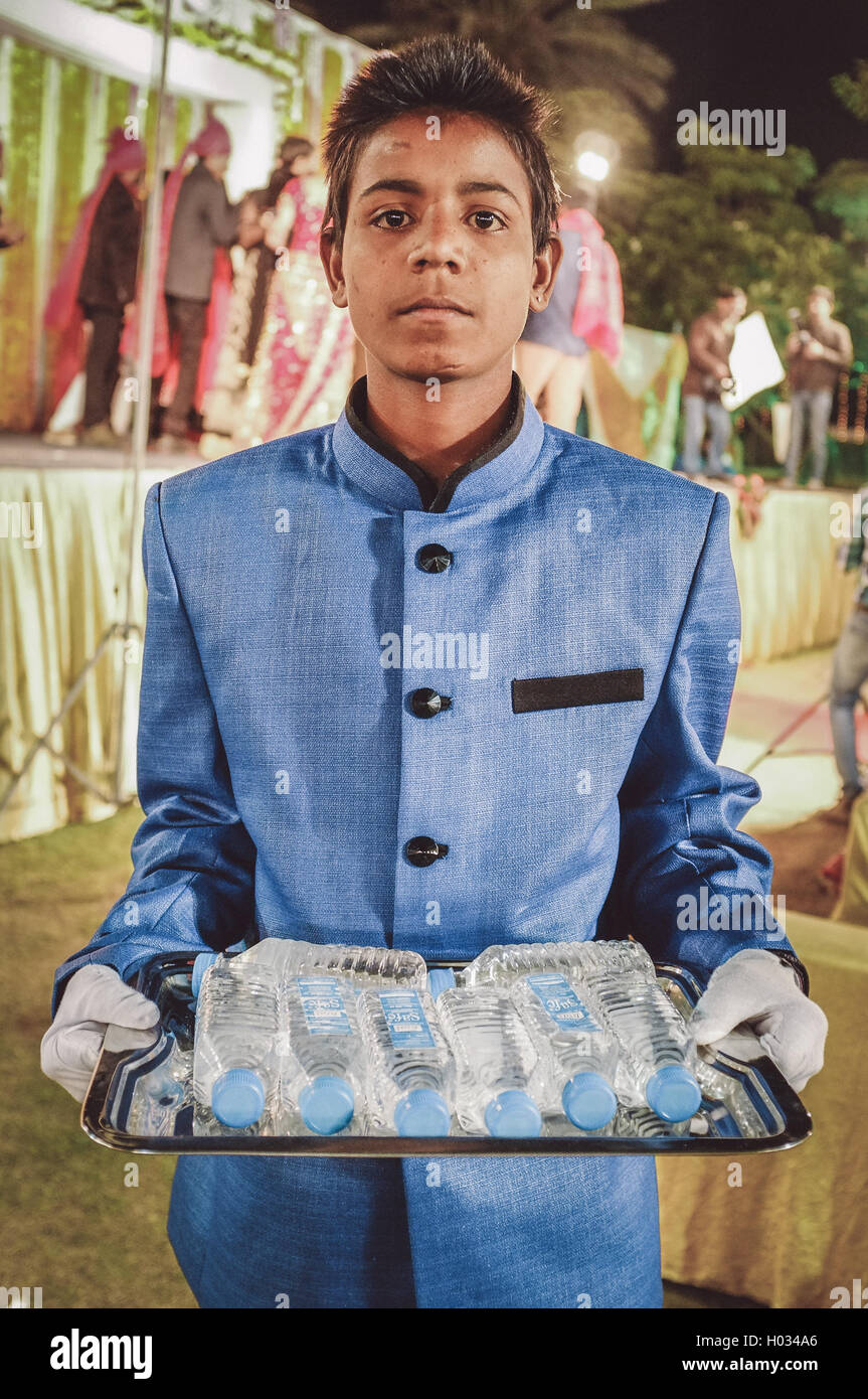 JODHPUR, INDIA - 08 FEBRUARY 2015: Young Indian boy wearing suit holds water bottles on tray working as waiter. Post-processed w Stock Photo