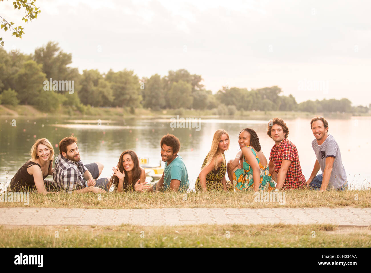 8 young good looking adults laying on grass close to lake in summerly feel Stock Photo