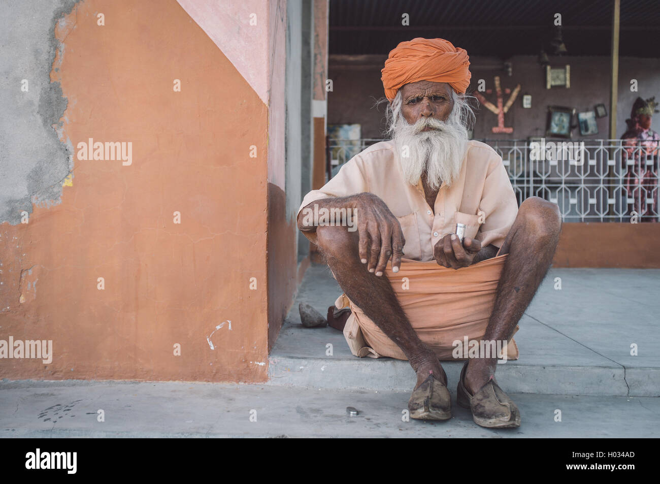 GODWAR, INDIA - 12 FEBRUARY 2015: Elderly Indian tribesman with turban in lungi sits on ground in front of temple. Post-processe Stock Photo