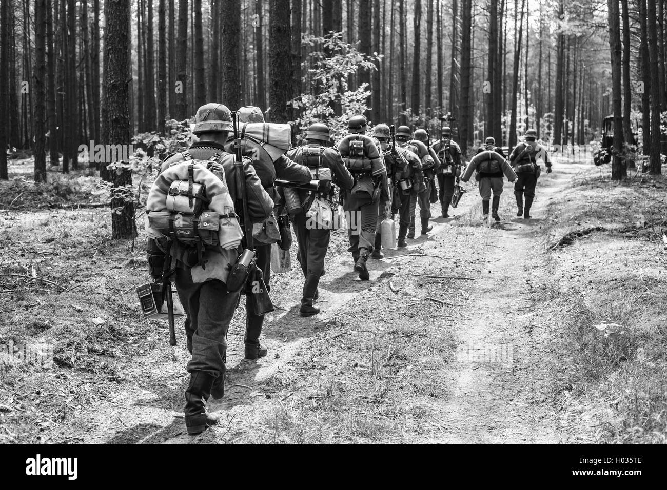 Unidentified Re-enactors Dressed As World War II German Soldiers Walks On Forest Road. Black And White Photography Stock Photo