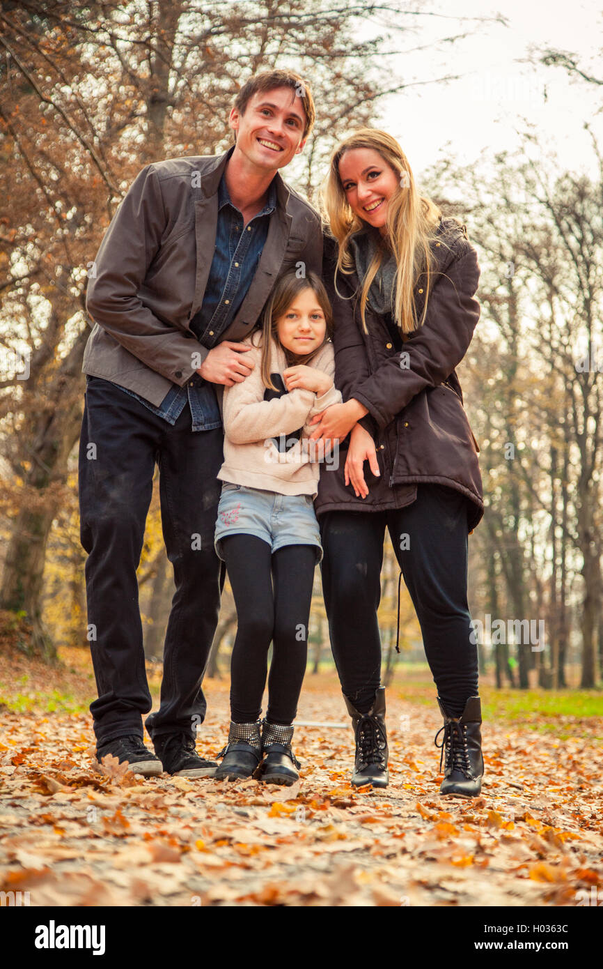 Family of three stand in park on an autumn day. Stock Photo