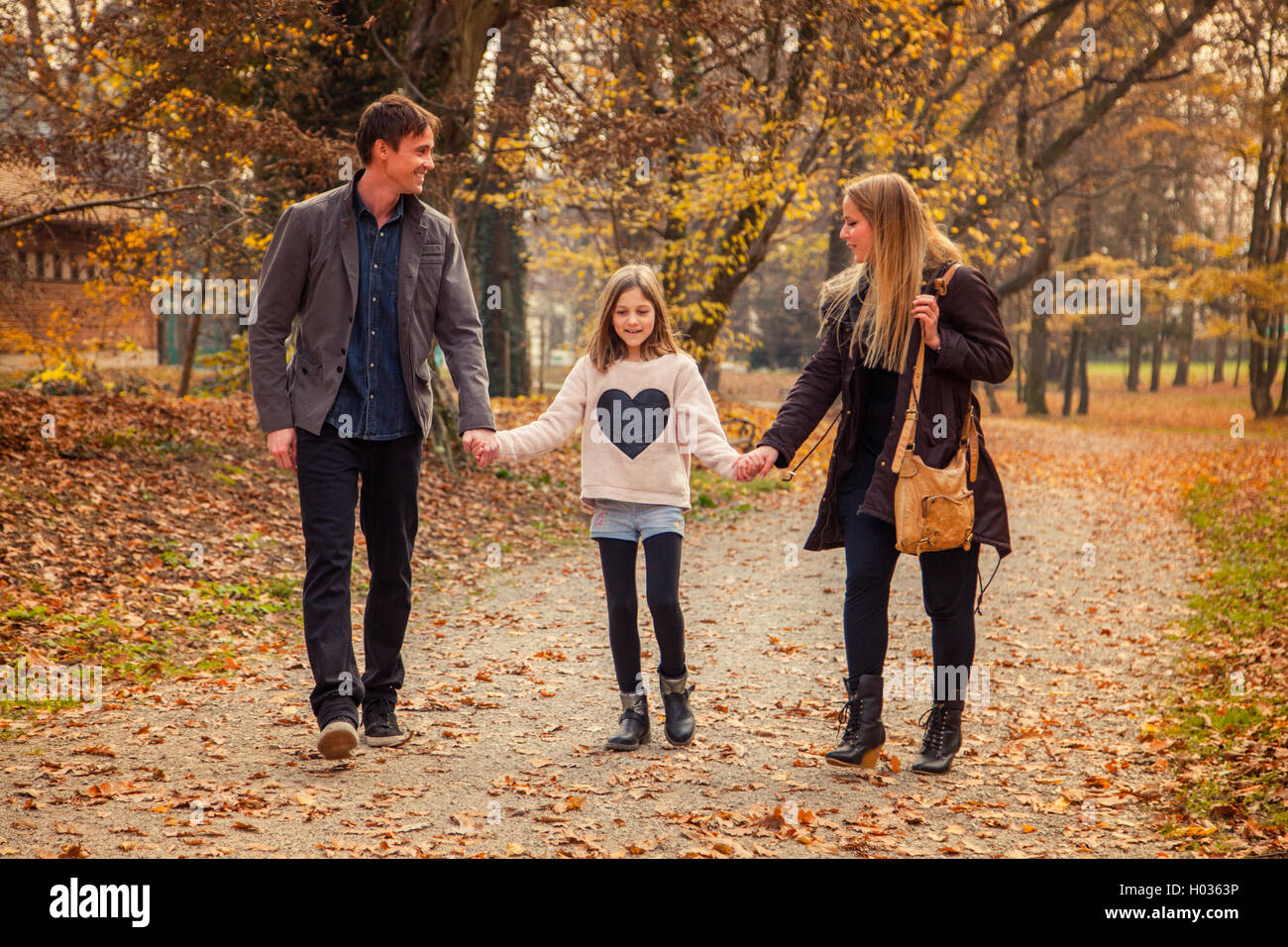 Family of three walk in a park on an autumn day. Stock Photo