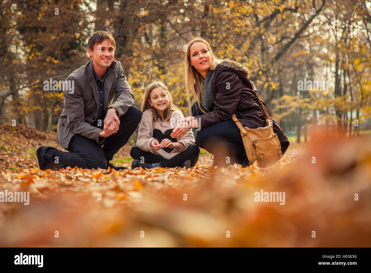 Family of three stand in park on an autumn day. Stock Photo