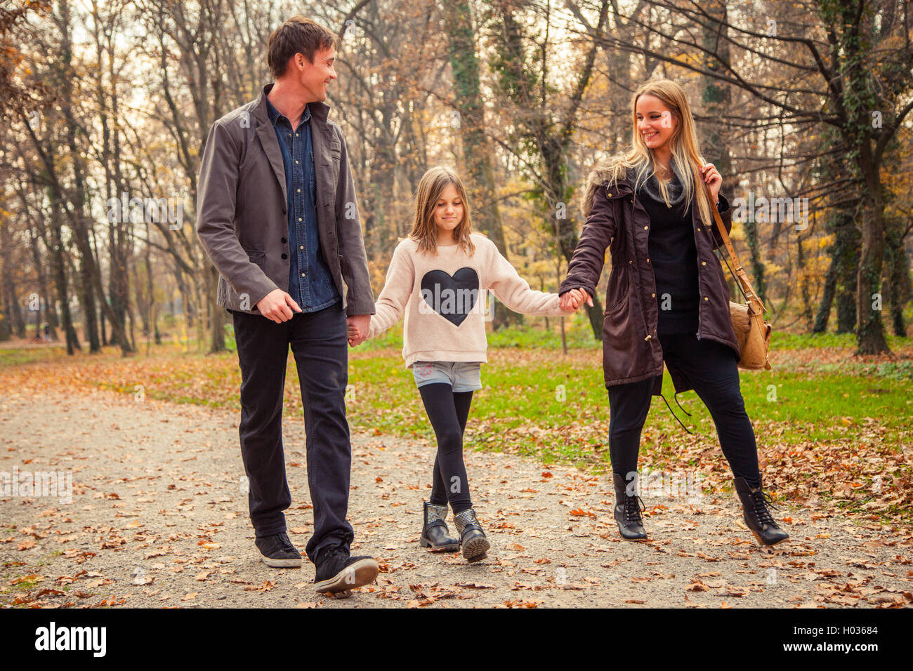 Family of three walk in a park on an autumn day. Stock Photo