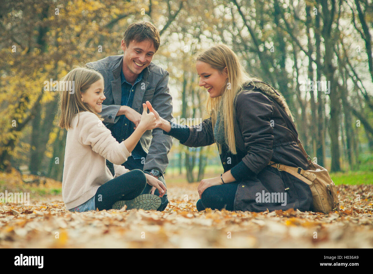 Family of three kneel in park on an autumn day. Stock Photo
