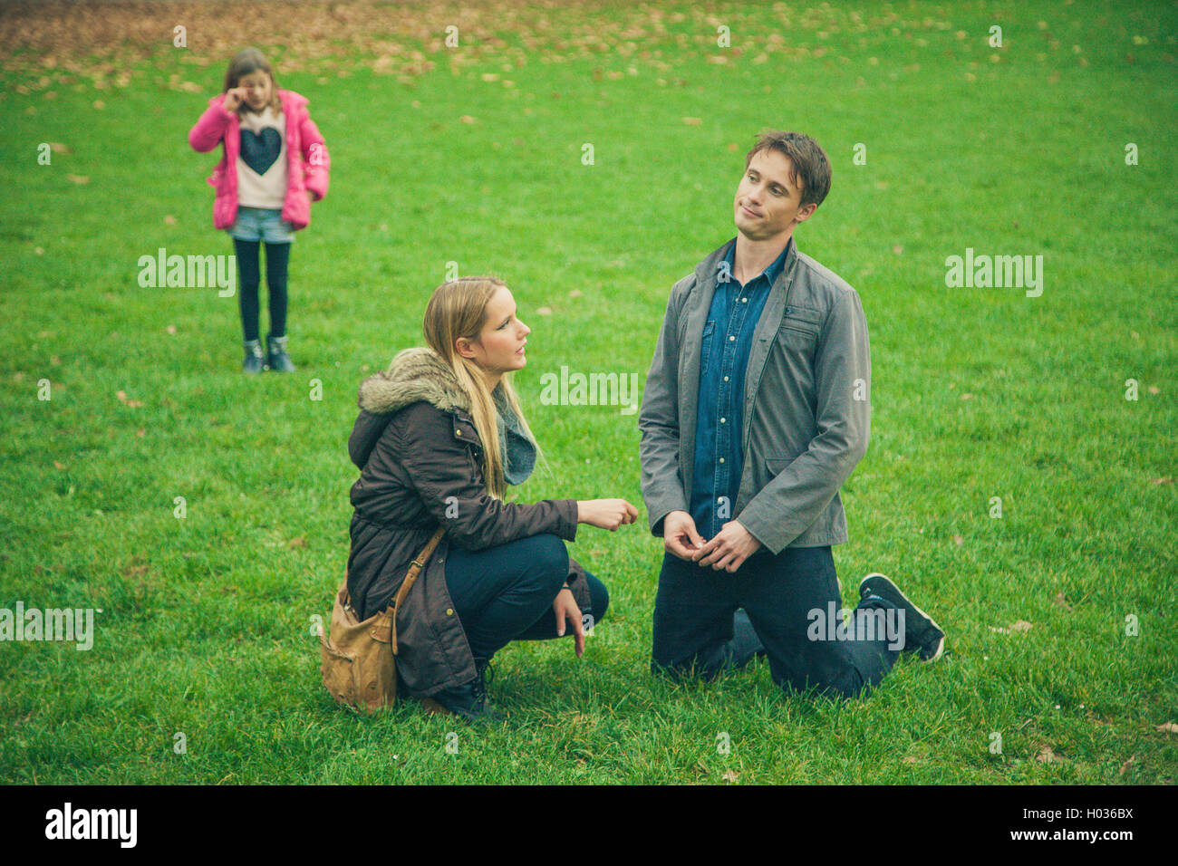 Family of three in park. Daughter cries close by to worried parents. Stock Photo