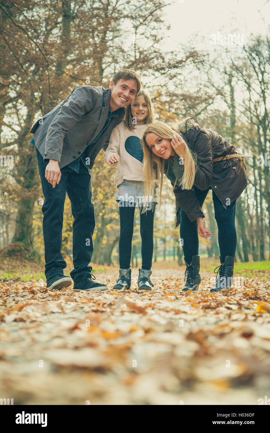 Family of three stand in park on an autumn day. Stock Photo