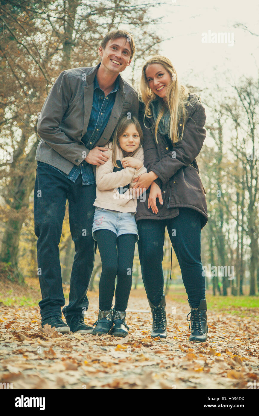 Family of three stand in park on an autumn day. Stock Photo