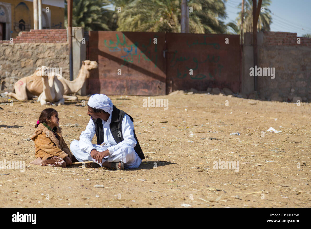 DARAW, EGYPT - FEBRUARY 6, 2016: Local camel salesmen and little girl sitting on the ground at camel market. Stock Photo