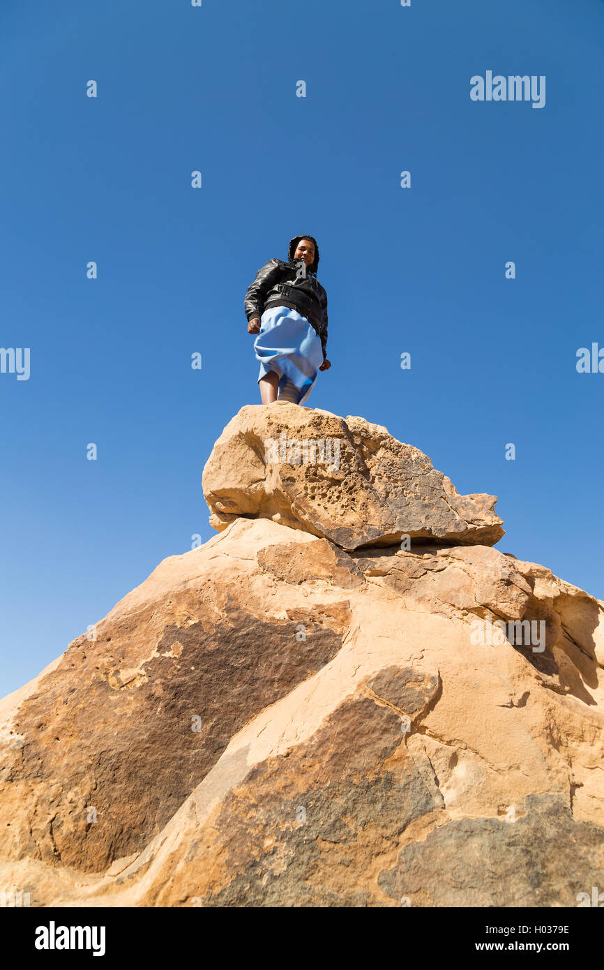 ASWAN, EGYPT - FEBRUARY 7, 2016: Local tourist standing on big rock in desert, Egypt. Stock Photo