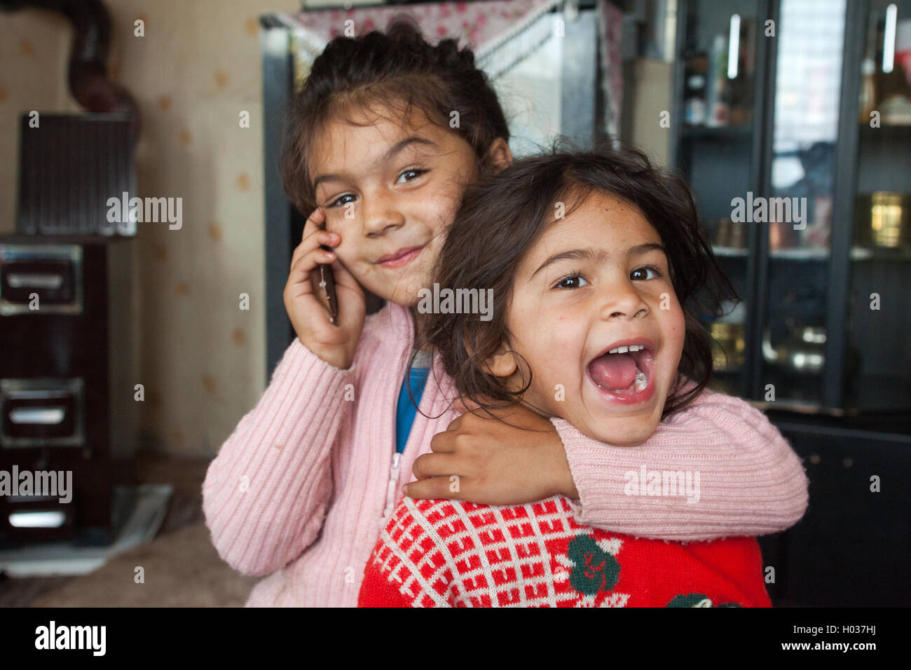 ZAGREB, CROATIA - OCTOBER 21, 2013: Portrait of little Roma girl hugging her sister and holding mobile phone. Stock Photo