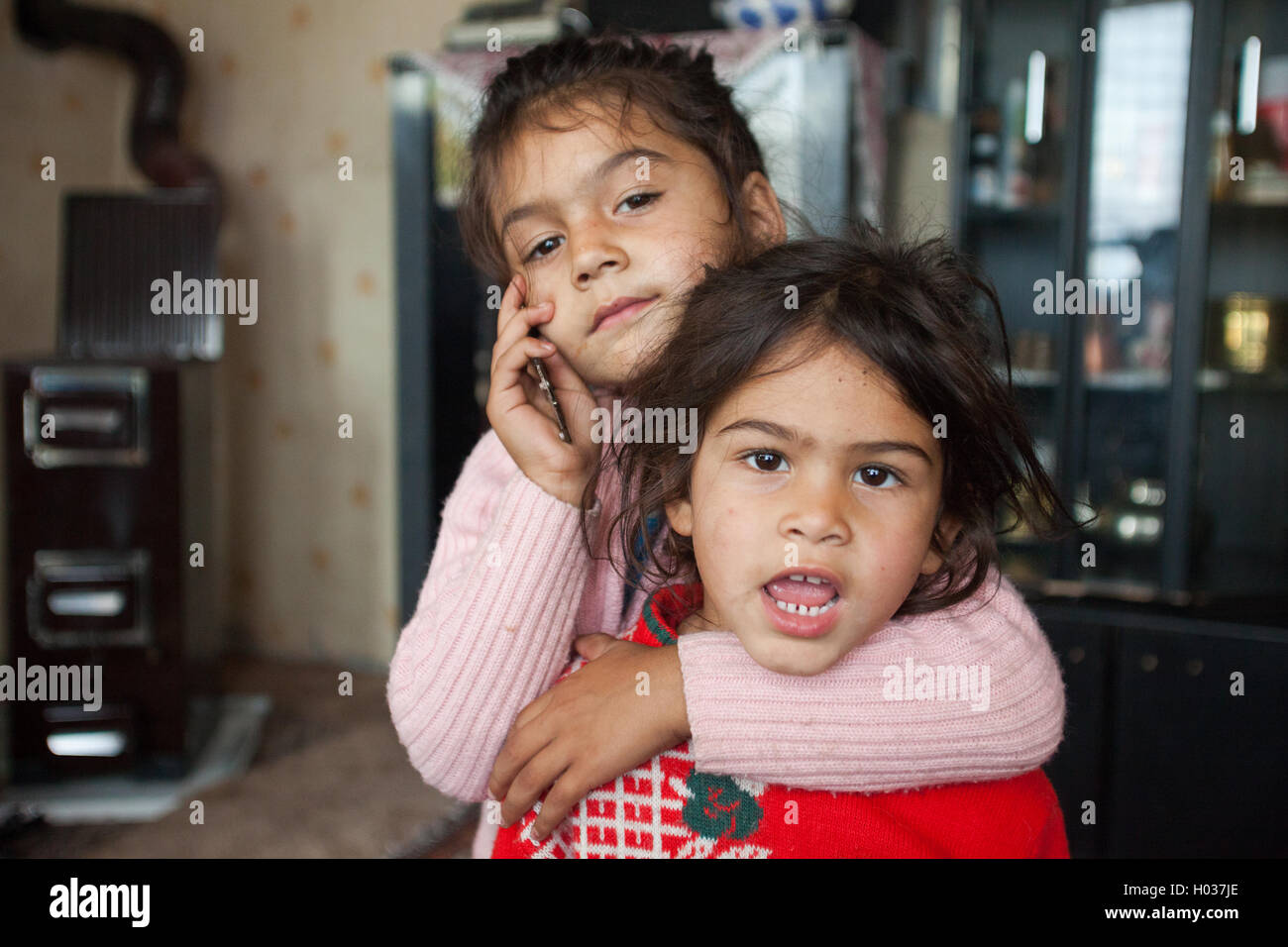 ZAGREB, CROATIA - OCTOBER 21, 2013: Portrait of little Roma girl hugging her sister and holding mobile phone. Stock Photo