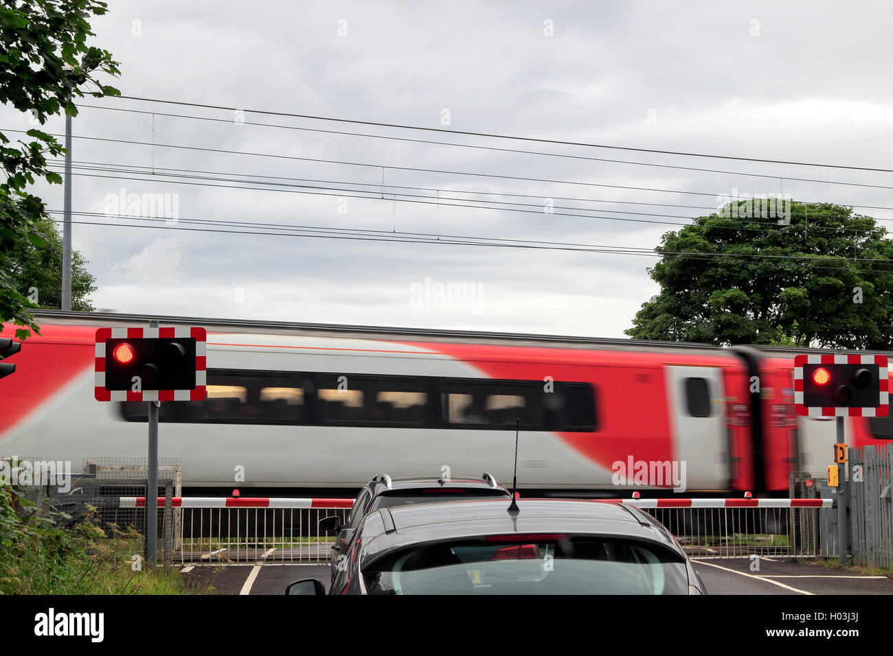 Train passing a level crossing with traffic waiting at the barrier, Northumberland, Northeast England, UK Stock Photo