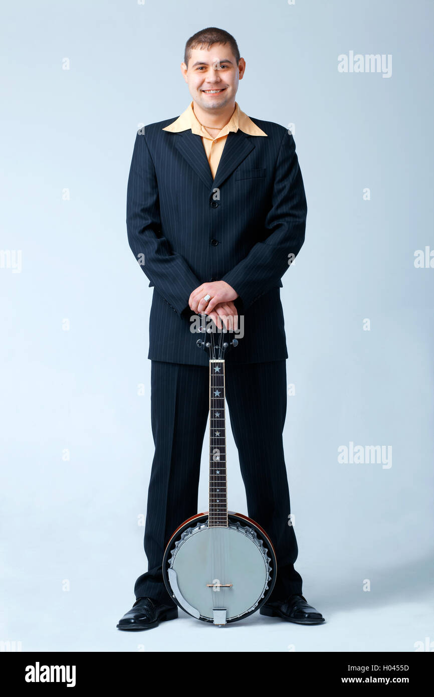 Man in dark suit standing with banjo, full length. Stock Photo