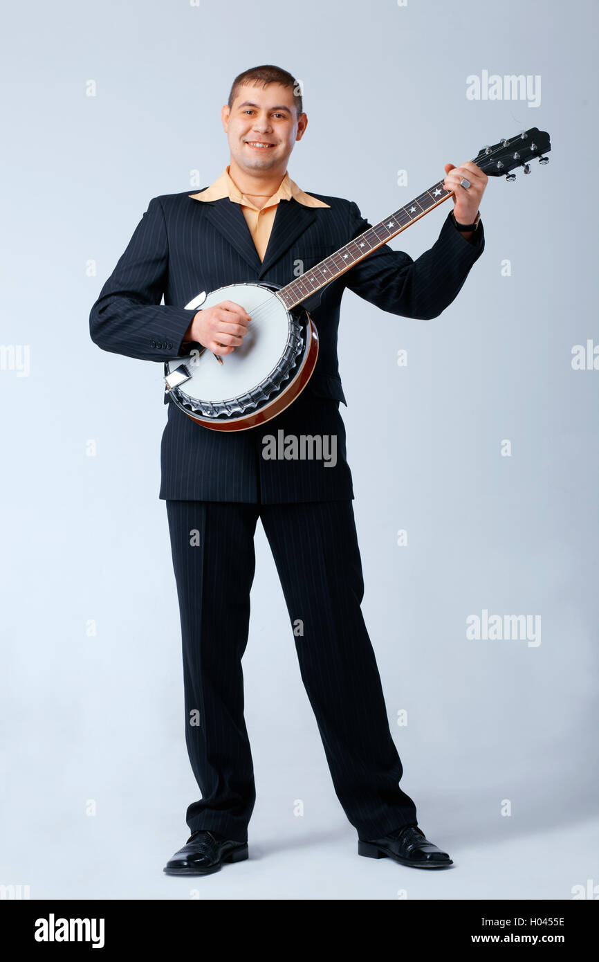 Man in suite is standing and playing on banjo against white, full length. Stock Photo