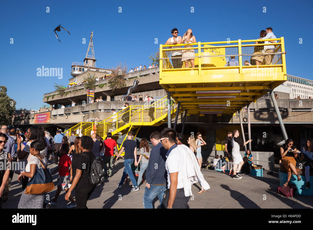 Crowds of people enjoying the sun outside the Royal Festival Hall on the Southbank of the Thames in London. Stock Photo
