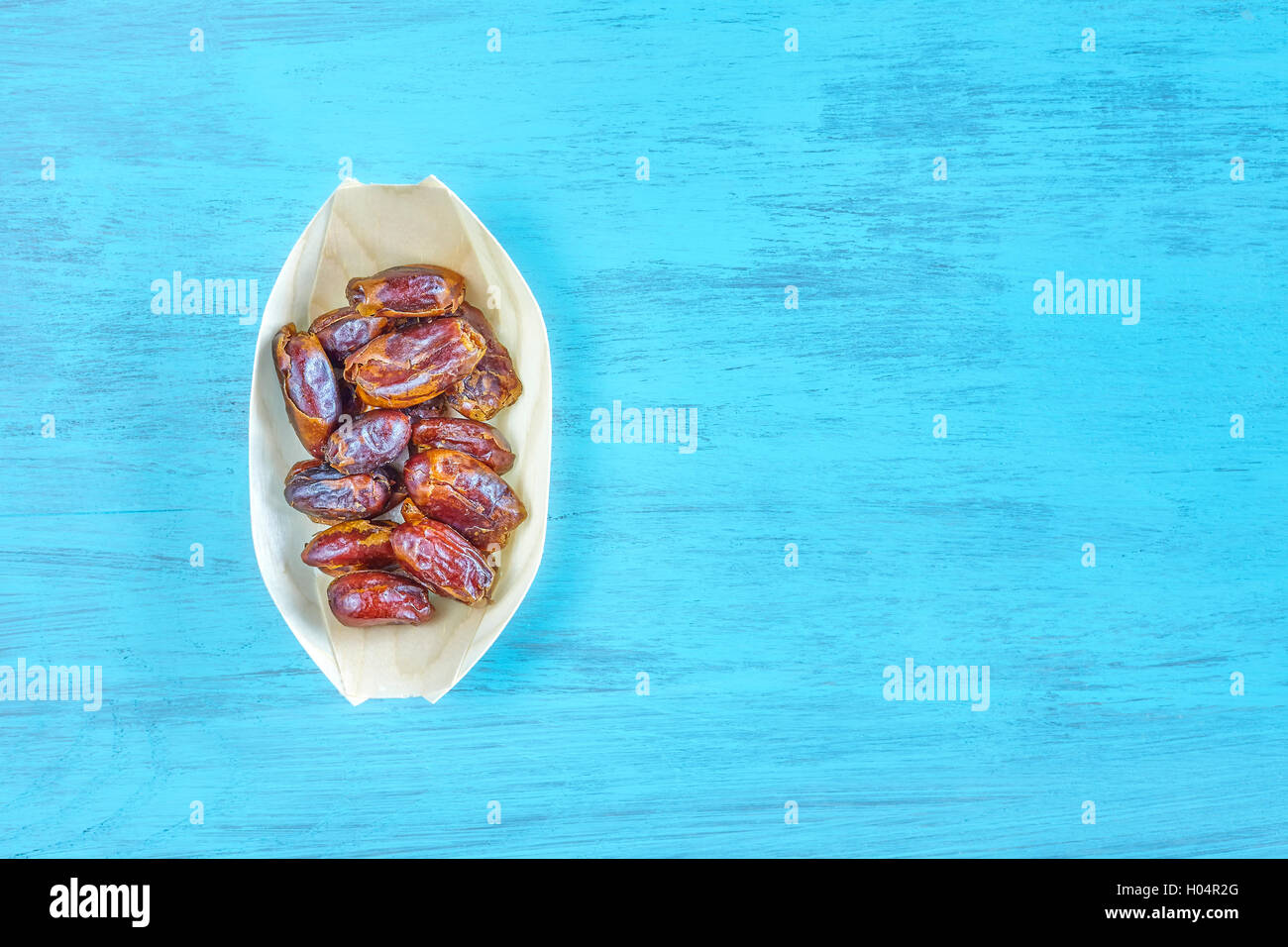 Dried dates in a wooden bowl on a rustic table, space for text, top view. Stock Photo