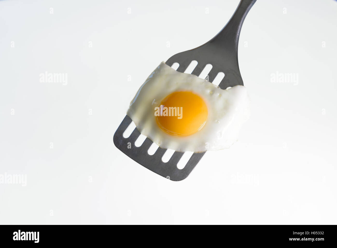 Fried egg on the steel spatula, ready to be served. White background