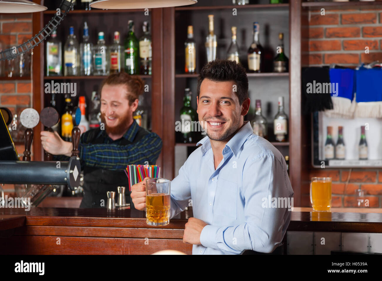 Young Man In Bar Hold Glasses Sit At Counter, Drinking Beer Stock Photo