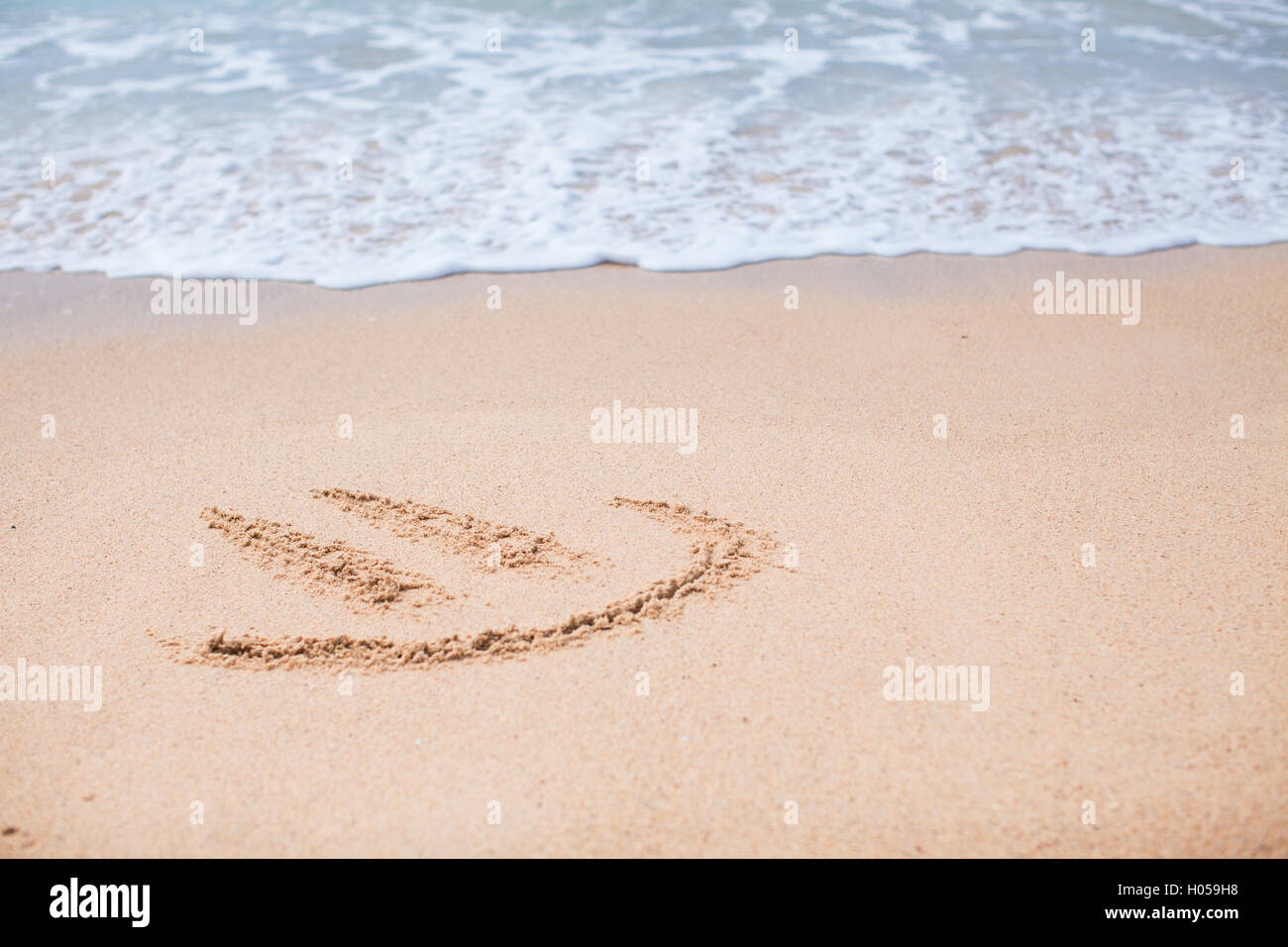 Happy smile drawing on the sand at tropical beach Stock Photo
