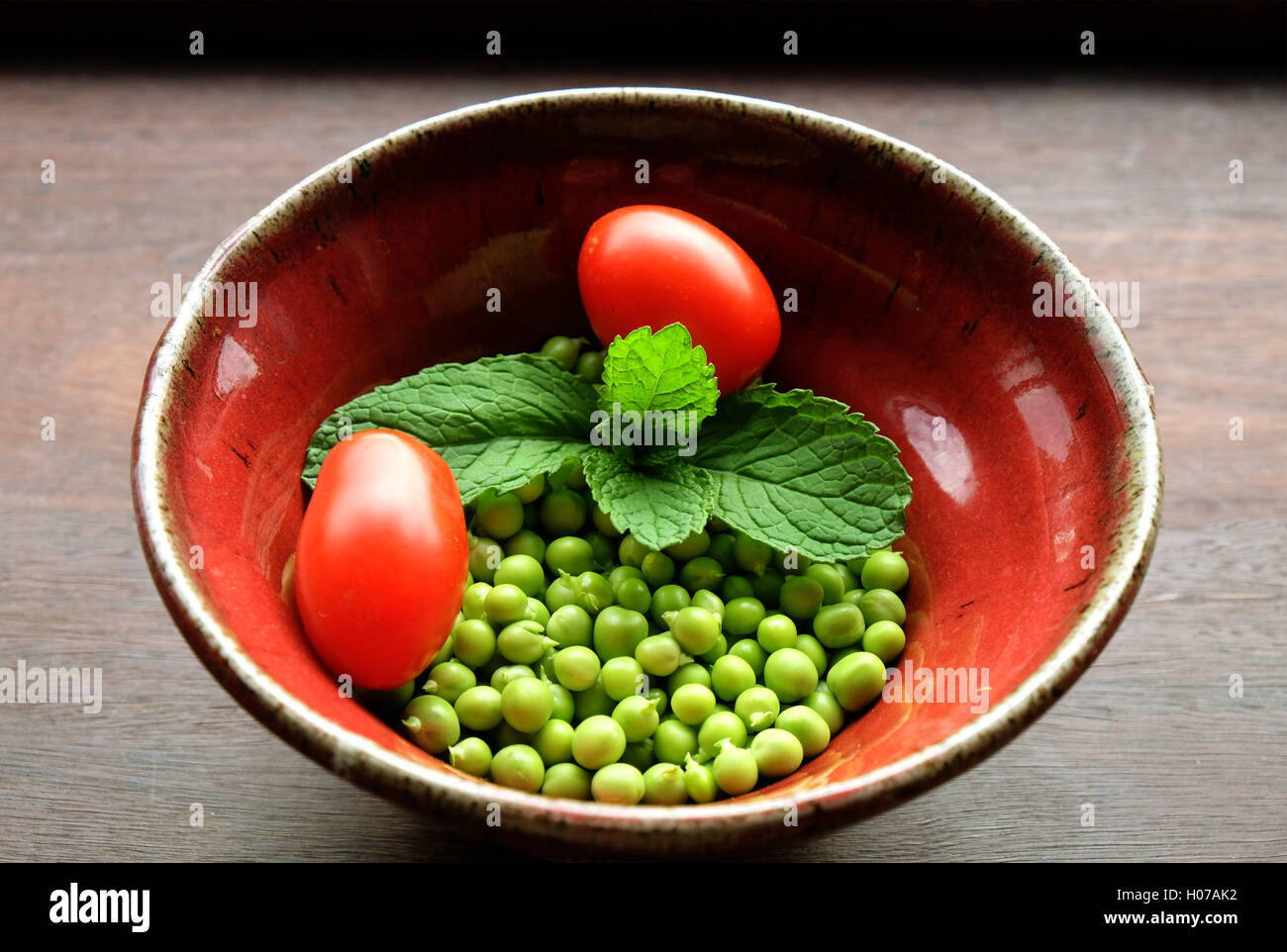 Fresh garden peas with mint and tomatoes in hand-thrown pottery bowl Stock Photo