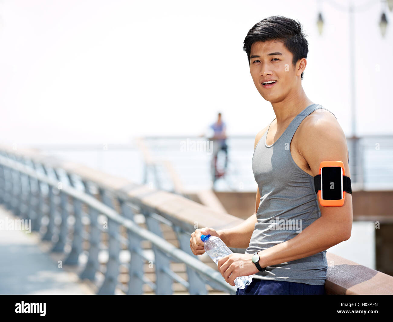 young asian man taking a break with a bottle of water in hands during outdoor exercise Stock Photo