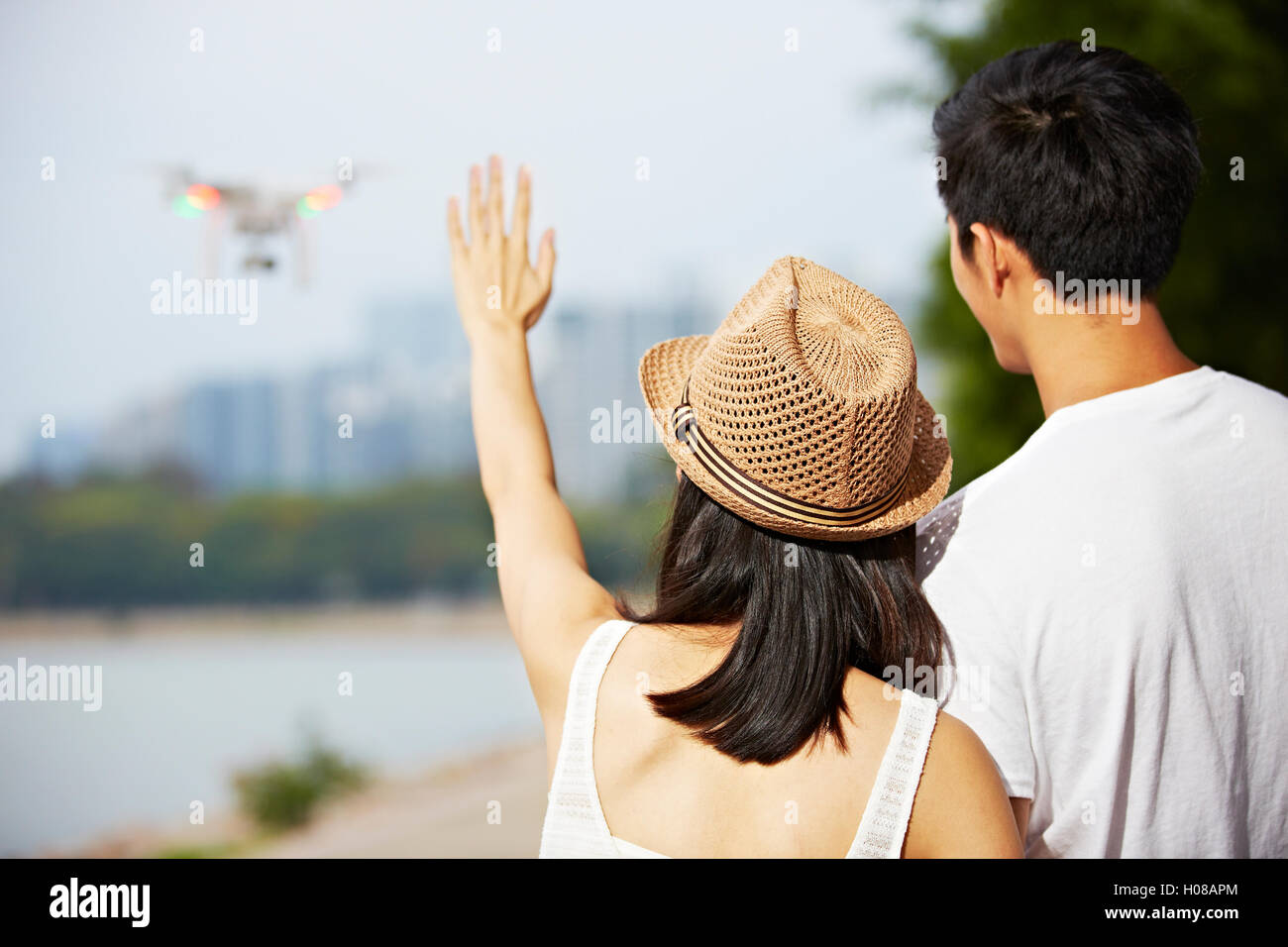 young asian woman waving to a flying drone operated by her friend or partner Stock Photo