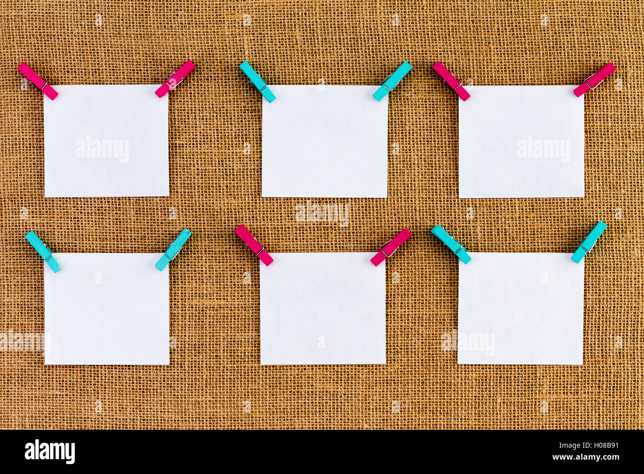 Six neatly aligned blank white notepads suspended from alternating blue and pink wooden clothespins over rustic burlap or hessia Stock Photo