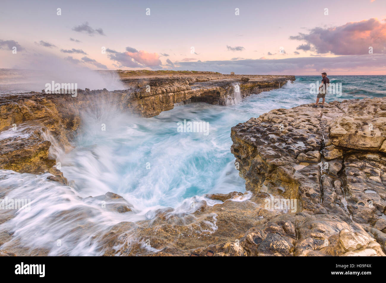 Hiker on the cliffs admires the crashing waves at Devil's Bridge, Antigua, Antigua and Barbuda, Leeward Islands, West Indies Stock Photo