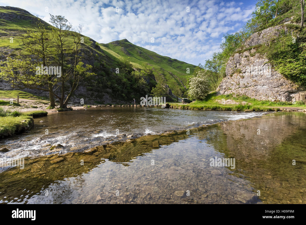 Dovedale reflections, hikers on stepping stones and Thorpe Cloud, limestone gorge in spring, Peak District, Derbyshire, UK Stock Photo