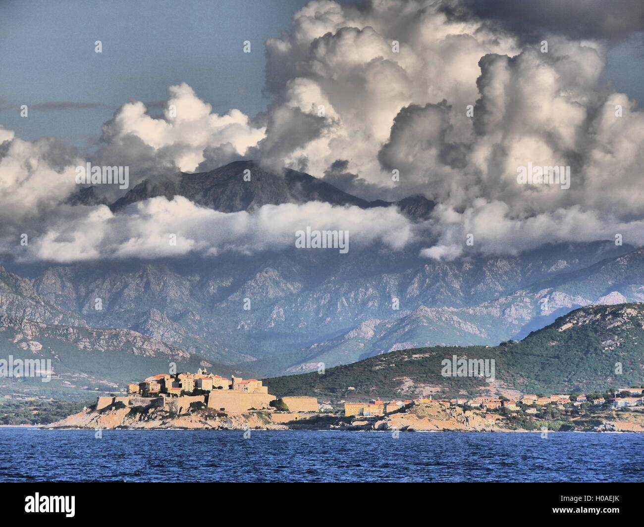 High contrast view from the sea of Corsica's Citadel with mountains and swirling clouds in background Stock Photo