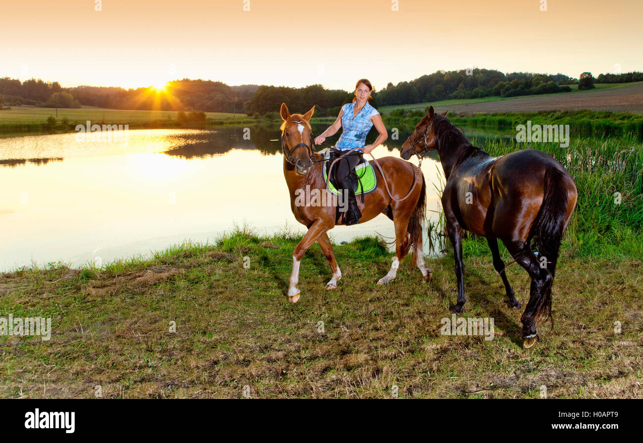 Woman with Two Horses by a Lake at Sunset Stock Photo