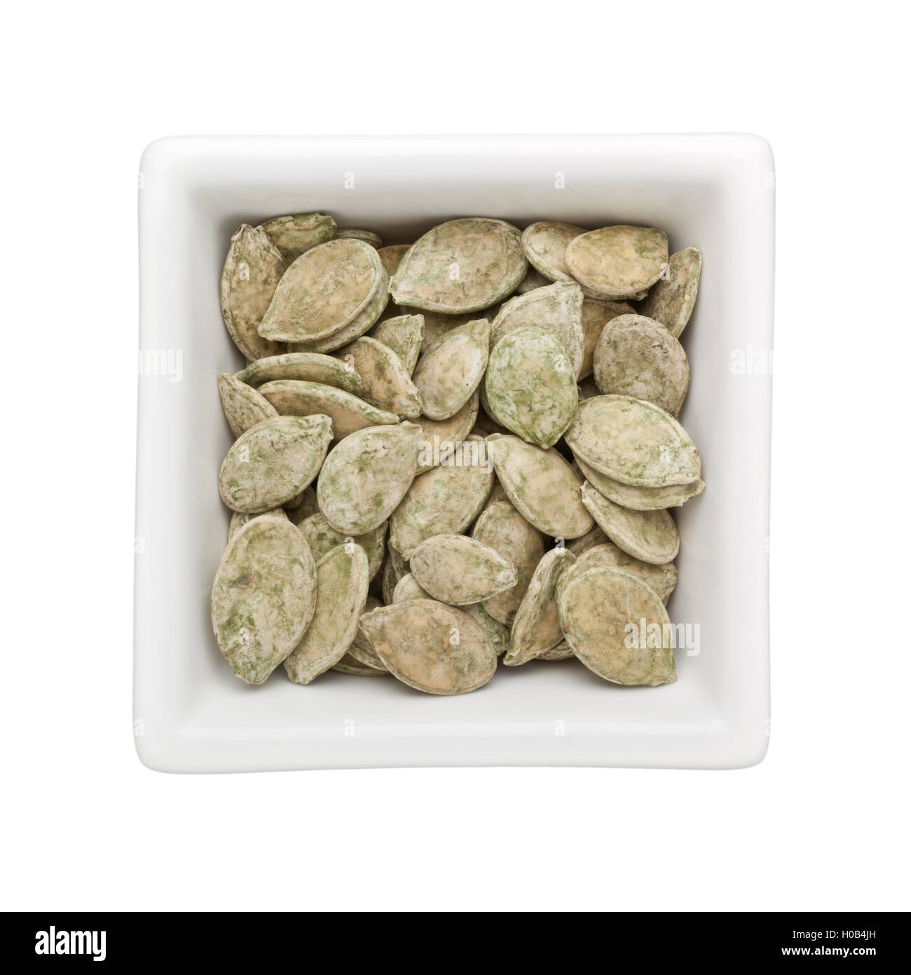 Green tea flavored roasted pumpkin seeds in a square bowl isolated on