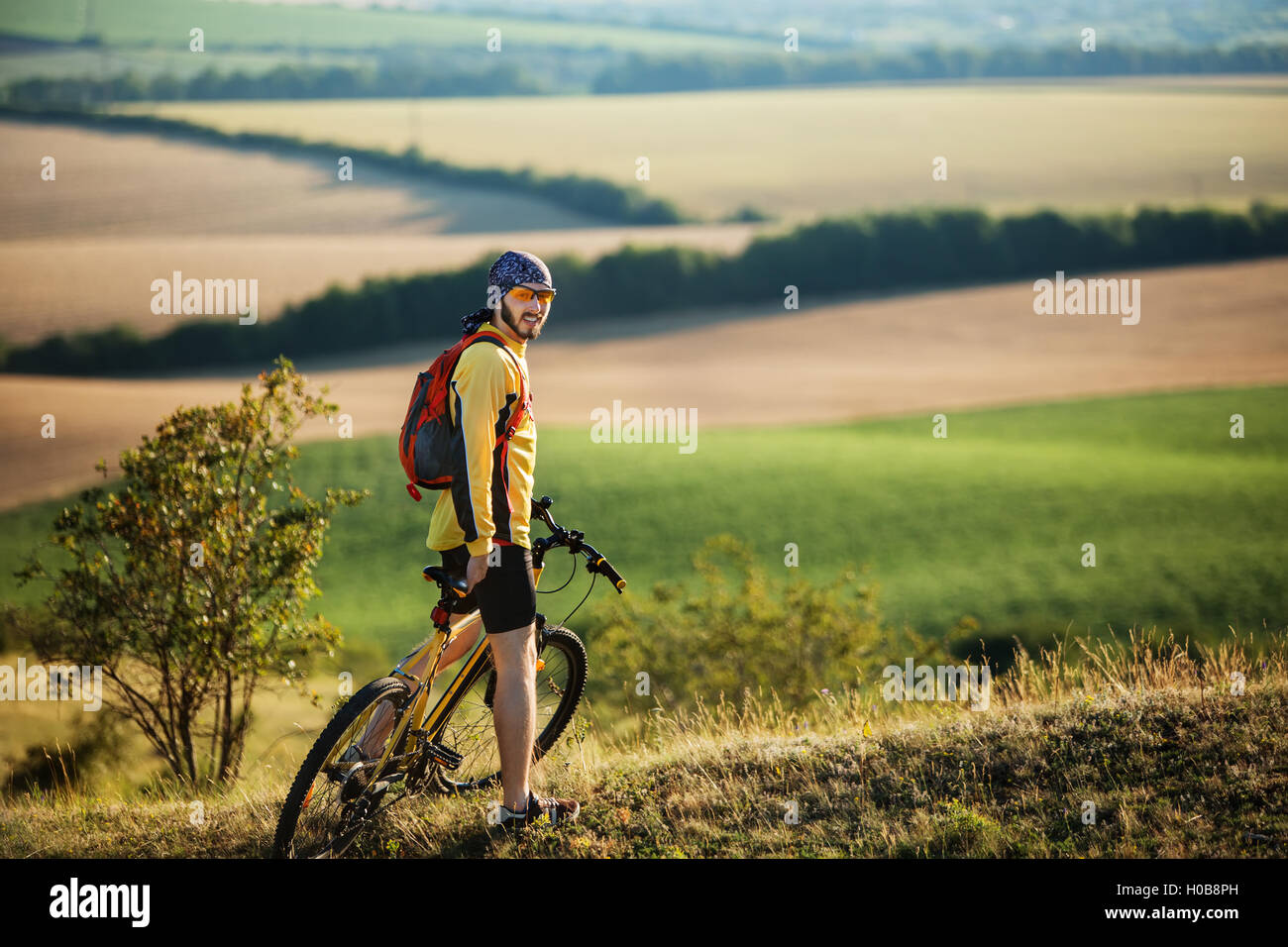 Young man cycling on a rural road through green summer meadow during