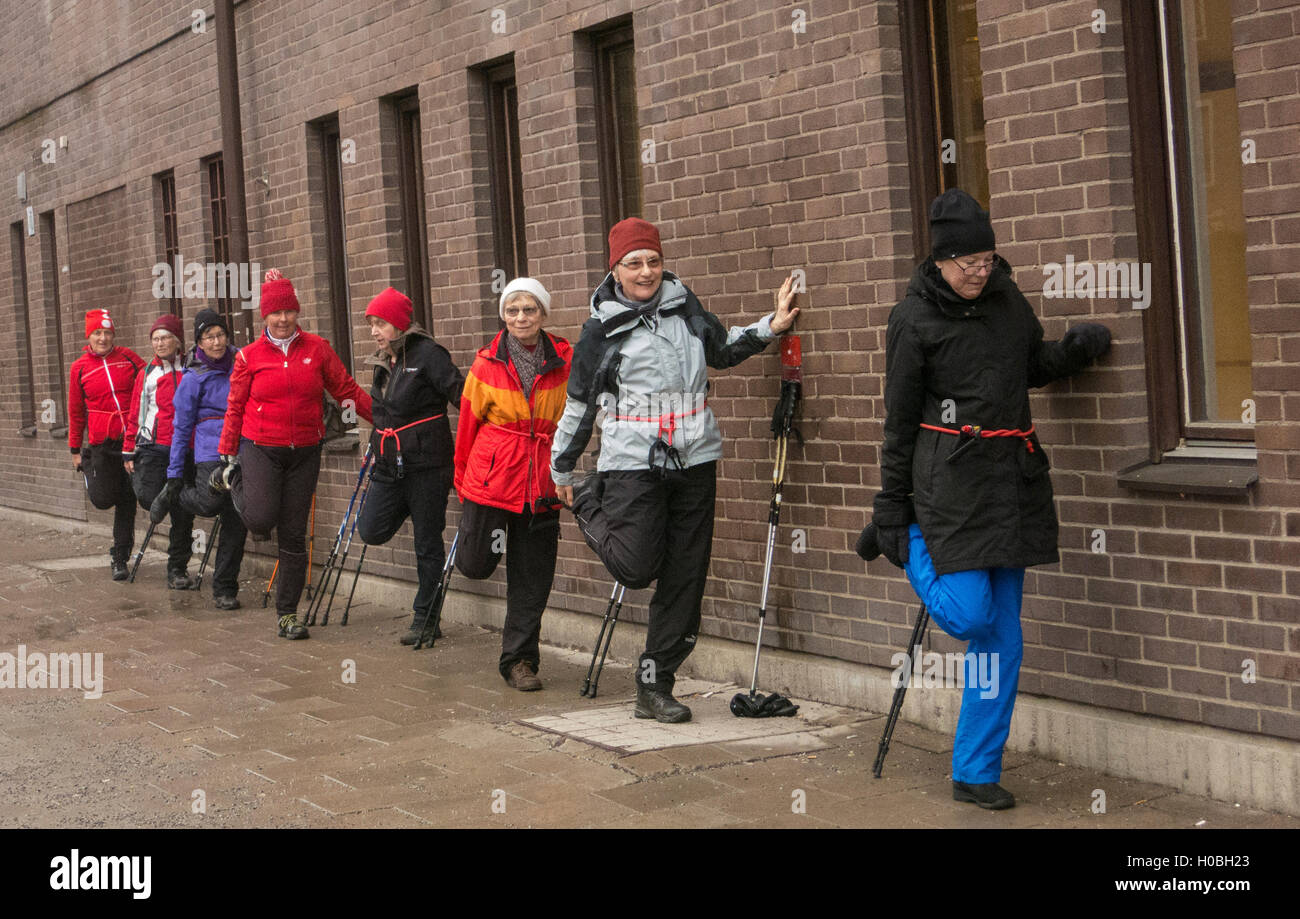 A walking group from Friskis&Svettis steading themselfs agains a brick building and stretch after a walking work-out with sticks Stock Photo