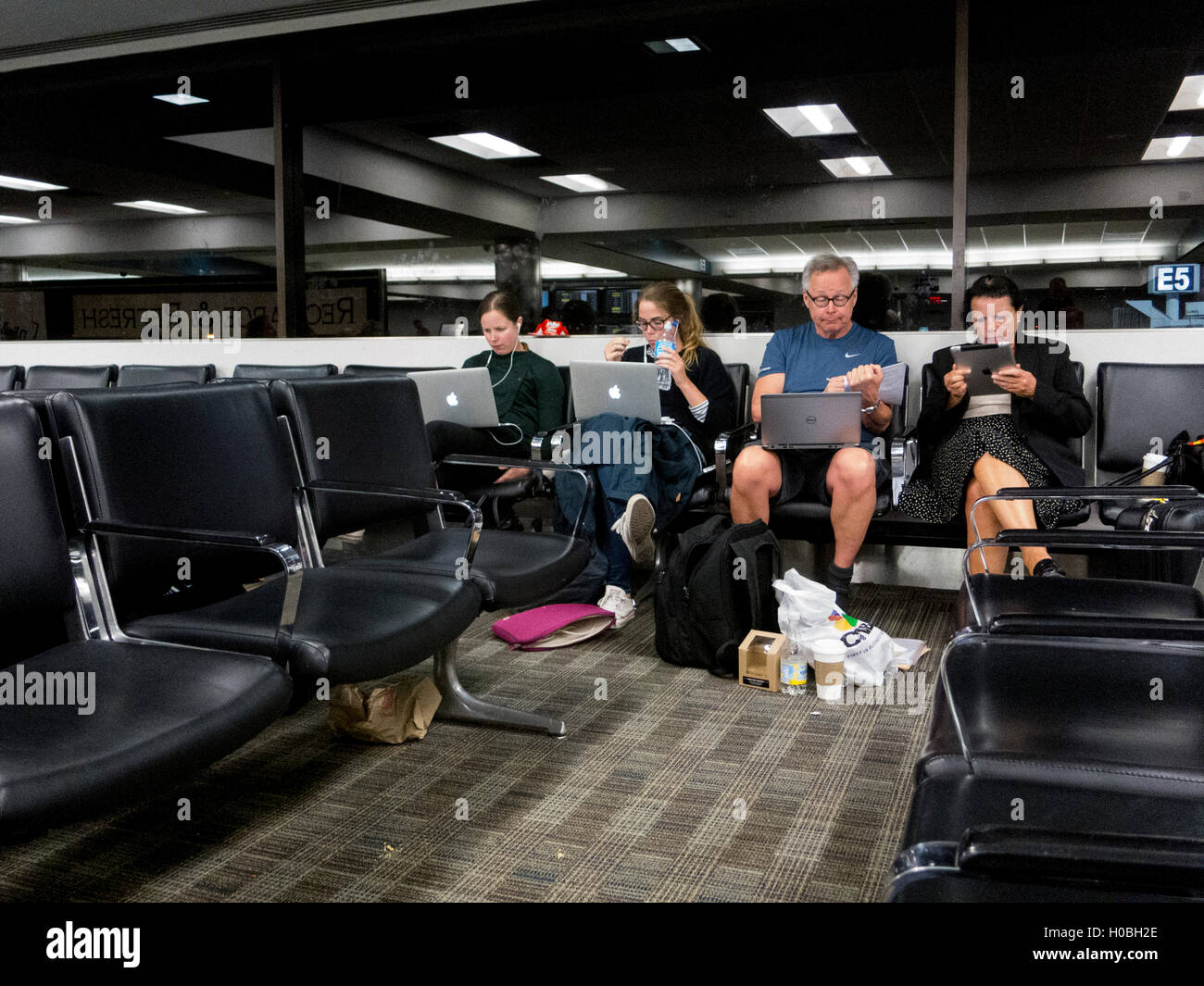 Passengers at Fort Lauderdale Hollywood airport busy with laptops while waiting. Stock Photo