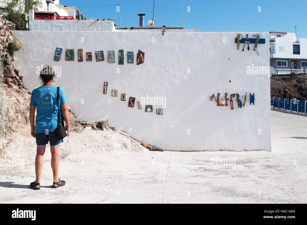 Fuerteventura: man looking at the words Hope, Illusion, Peace and Cheerfulness composed in Spanish by pieces of old boats on a wall in El Cotillo Stock Photo