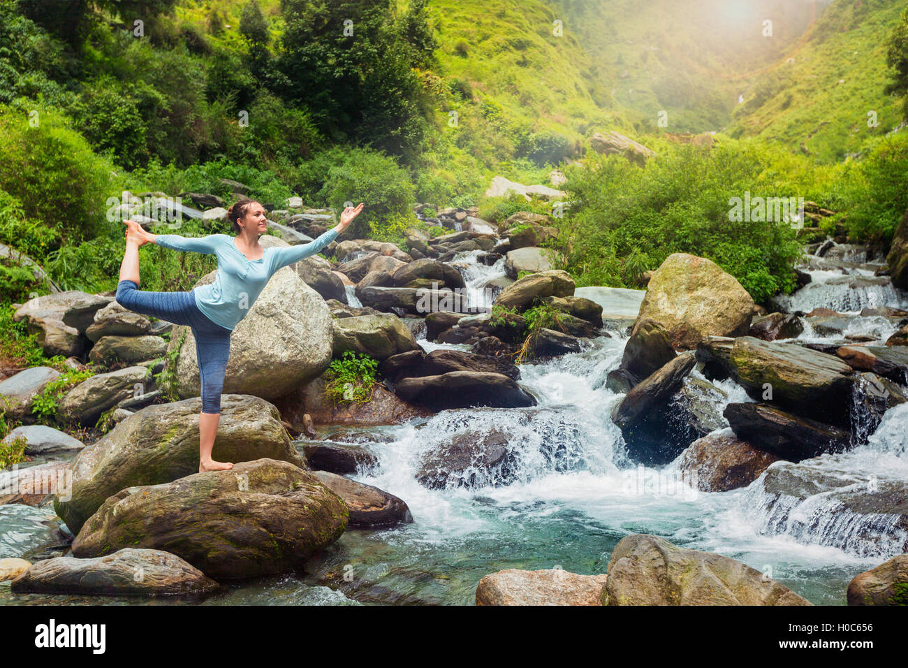 Woman doing yoga asana Natarajasana outdoors at waterfall Stock Photo