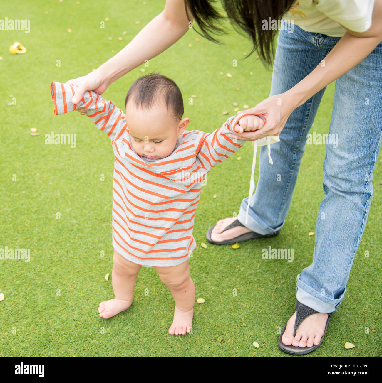 Asian Mother Holding Baby Hand To Walk Training On The Green Glass H0C71Njpg