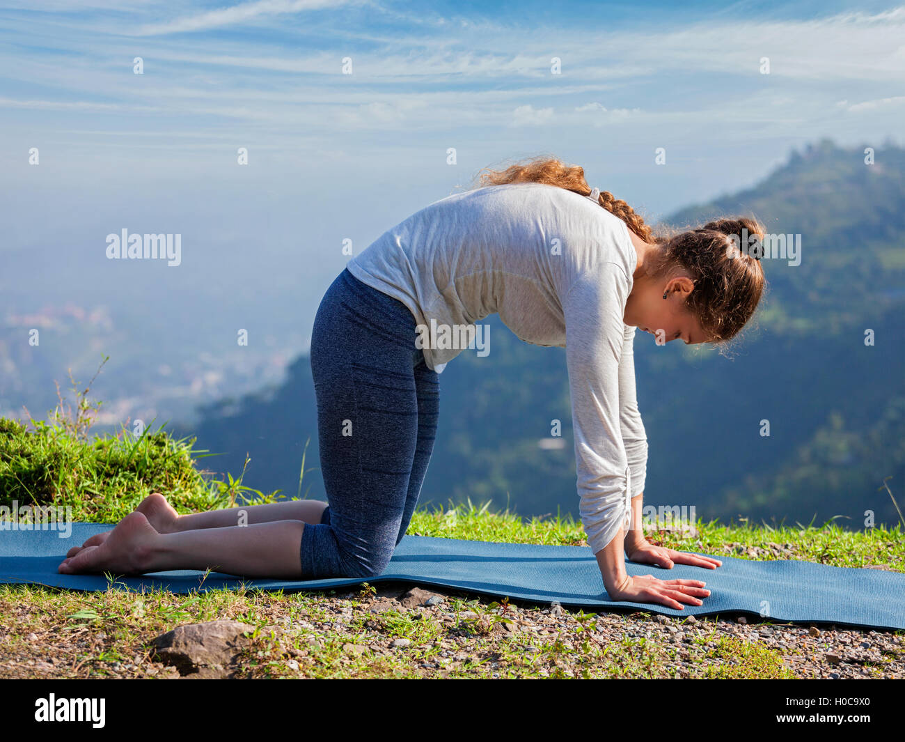 Sporty fit woman practices yoga asana Marjariasana outdoors Stock Photo