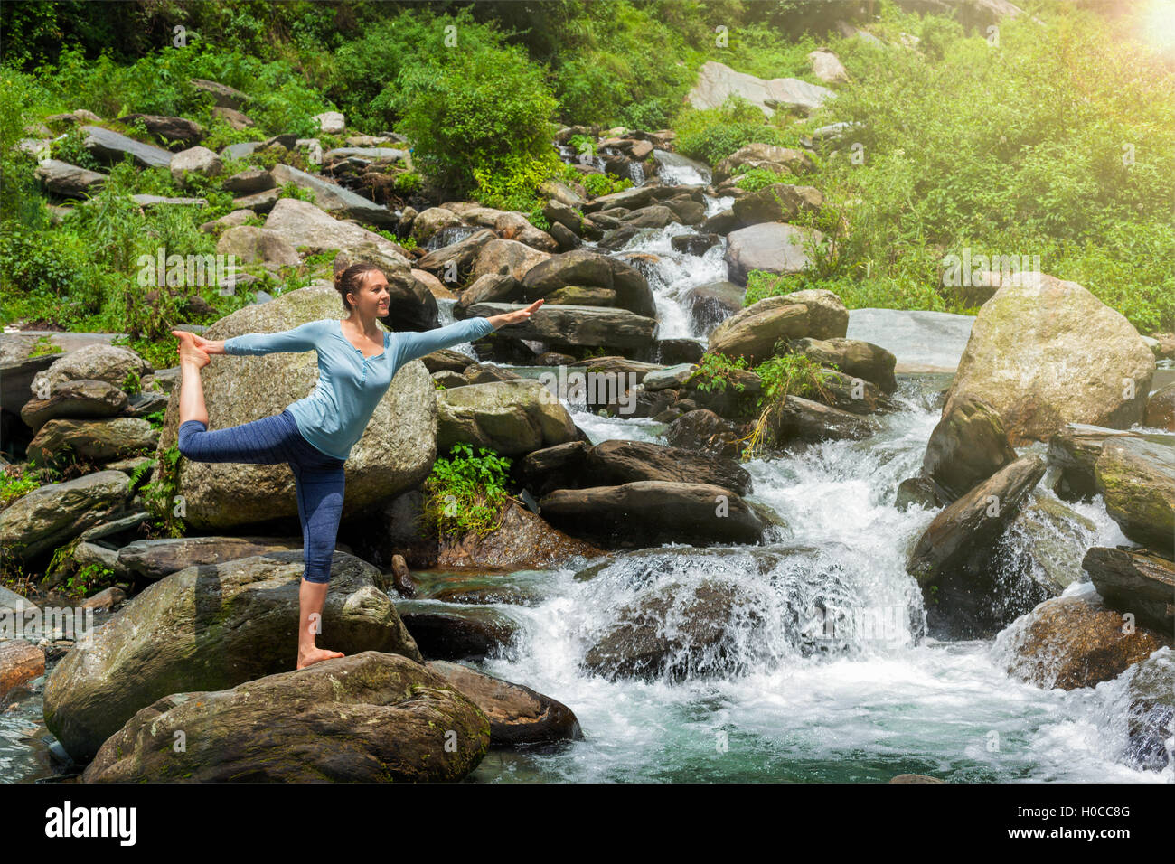 Woman doing yoga asana Natarajasana outdoors at waterfall Stock Photo