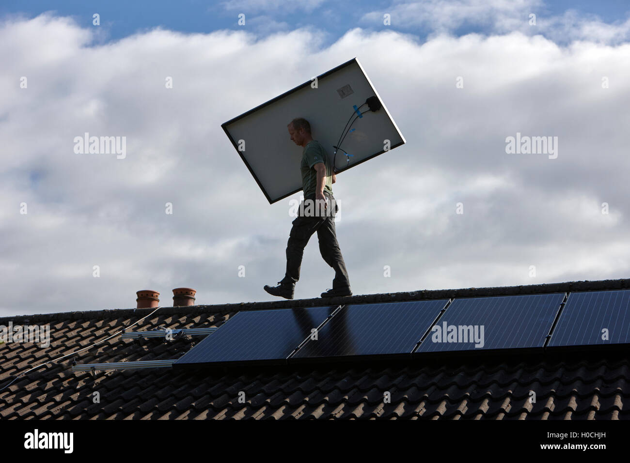 man installing rooftop solar panel array in a domestic solar panel installation in the uk Stock Photo