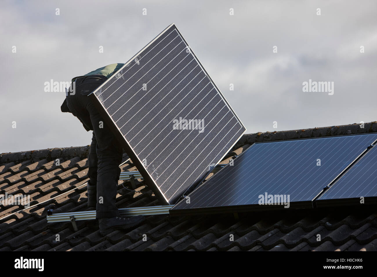 man installing rooftop solar panel array in a domestic solar panel installation in the uk Stock Photo