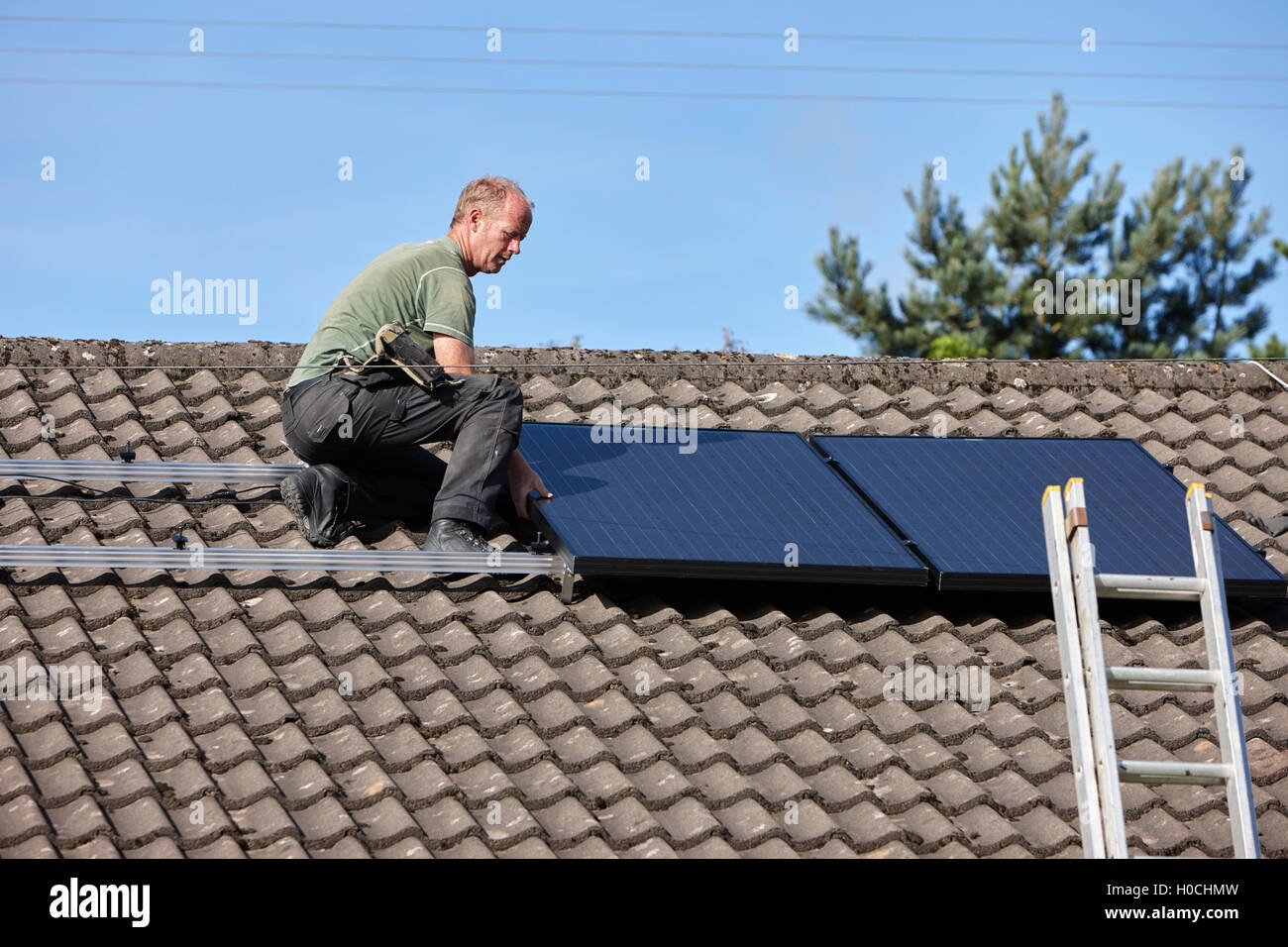 man installing rooftop solar panel array in a domestic solar panel installation in the uk Stock Photo