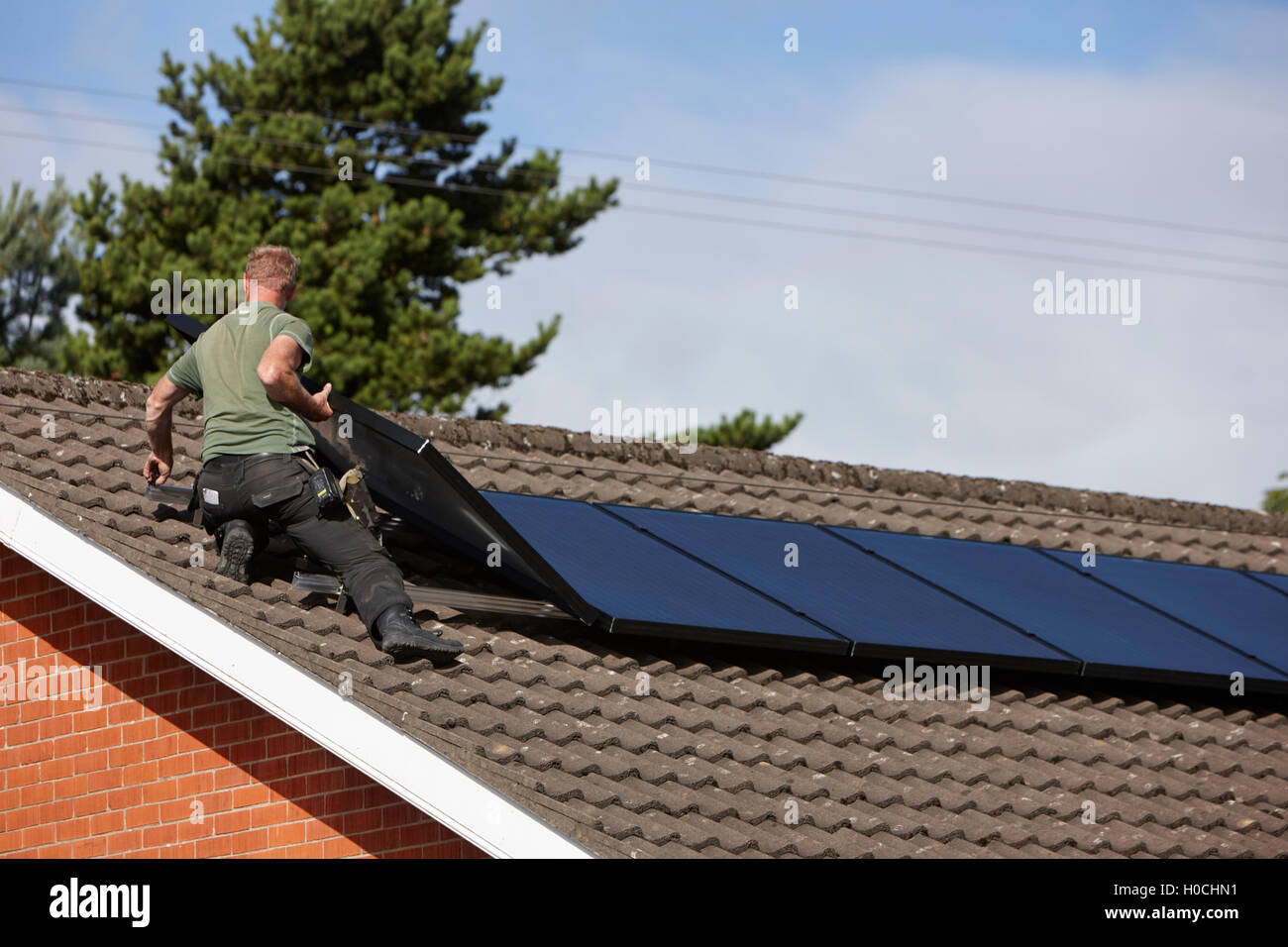 man installing rooftop solar panel array in a domestic solar panel installation in the uk Stock Photo