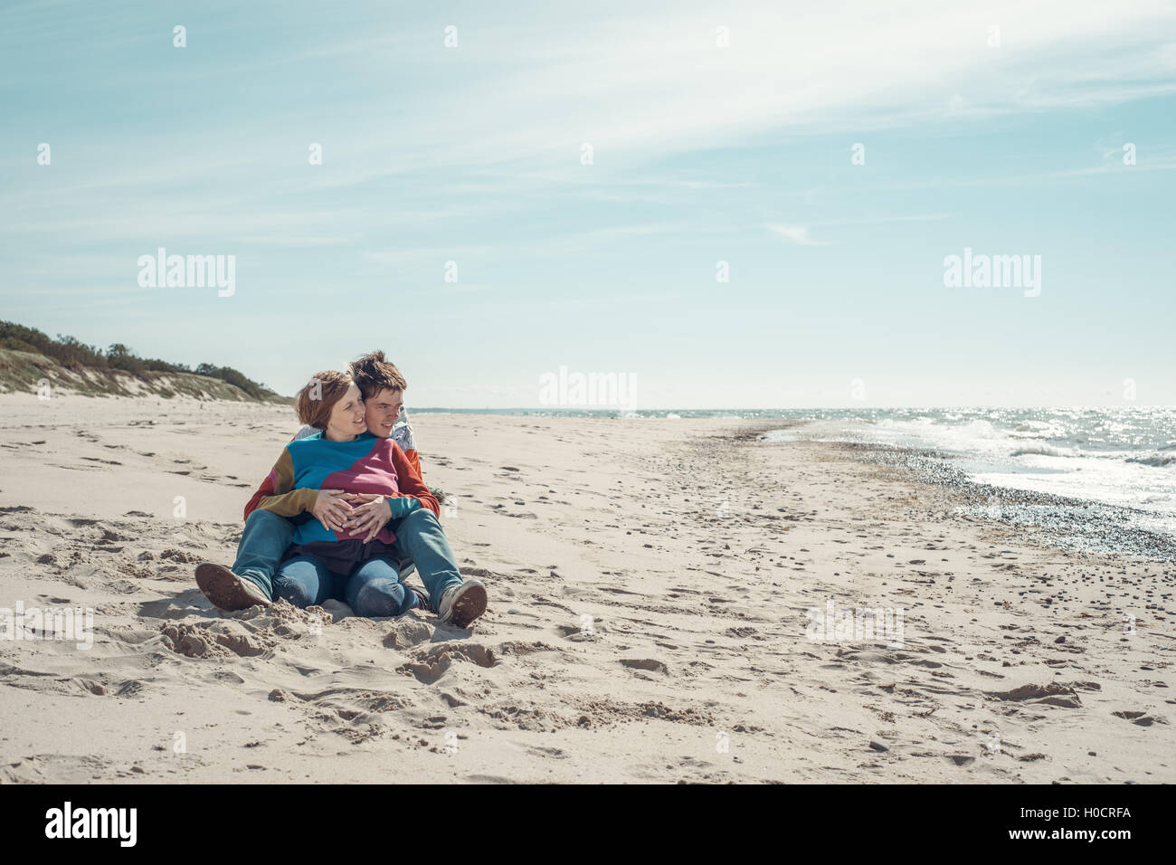 Young man embracing a woman sitting on the beach Stock Photo - Alamy