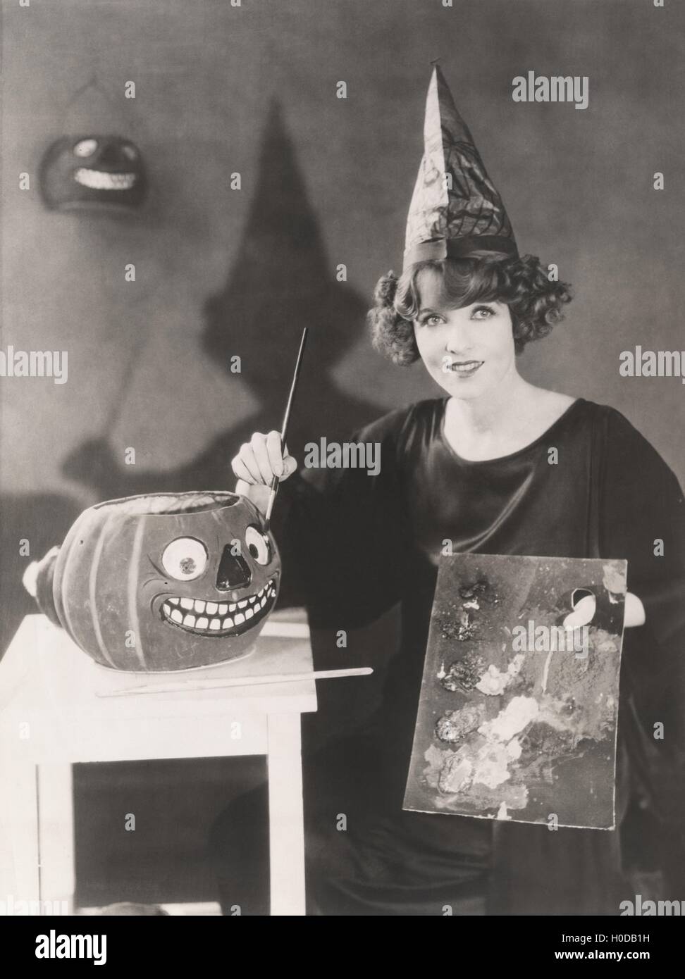 Woman in pointy hat painting a jack o'lantern Stock Photo